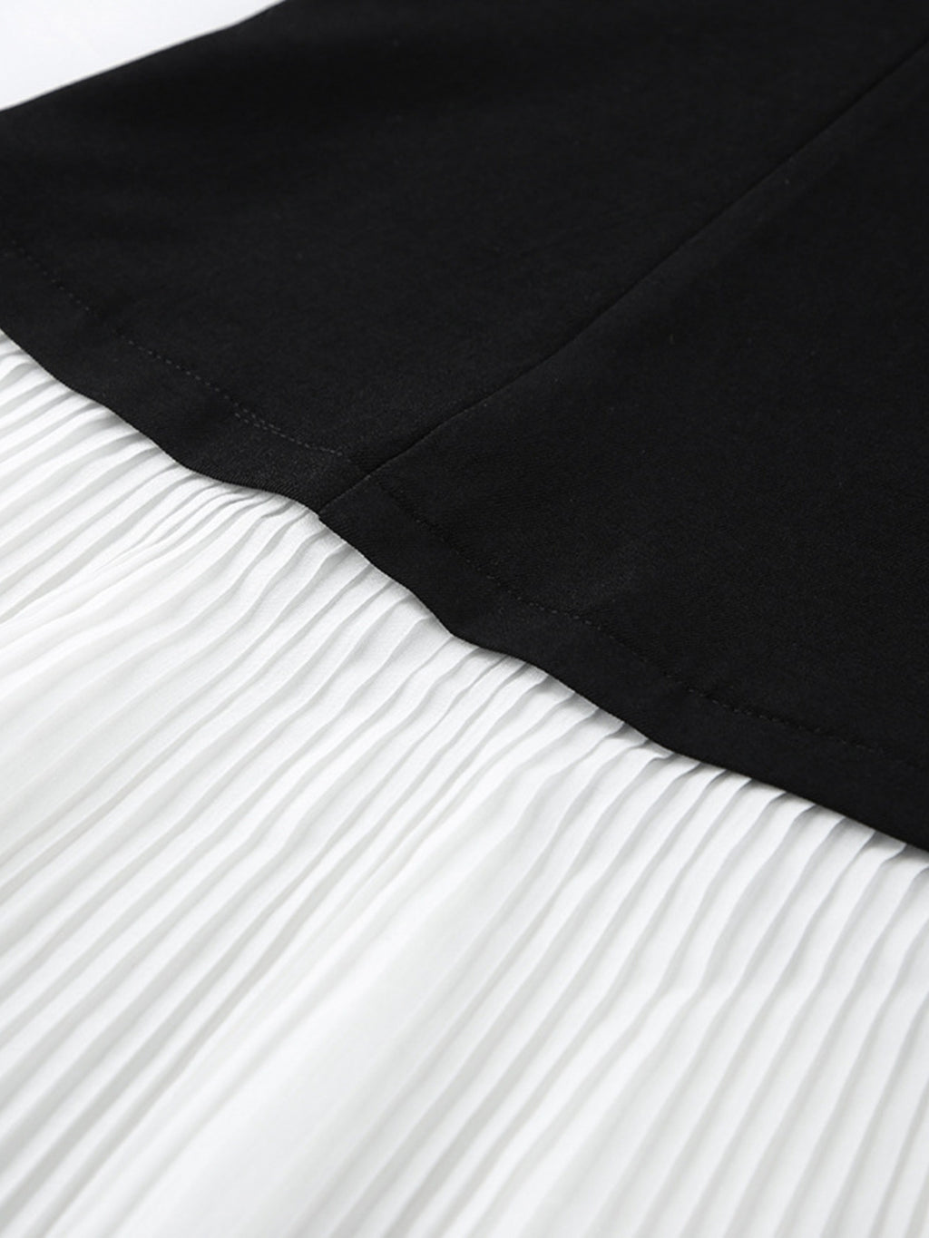 Black blazer dress with pleated skirt, close-up of seam line