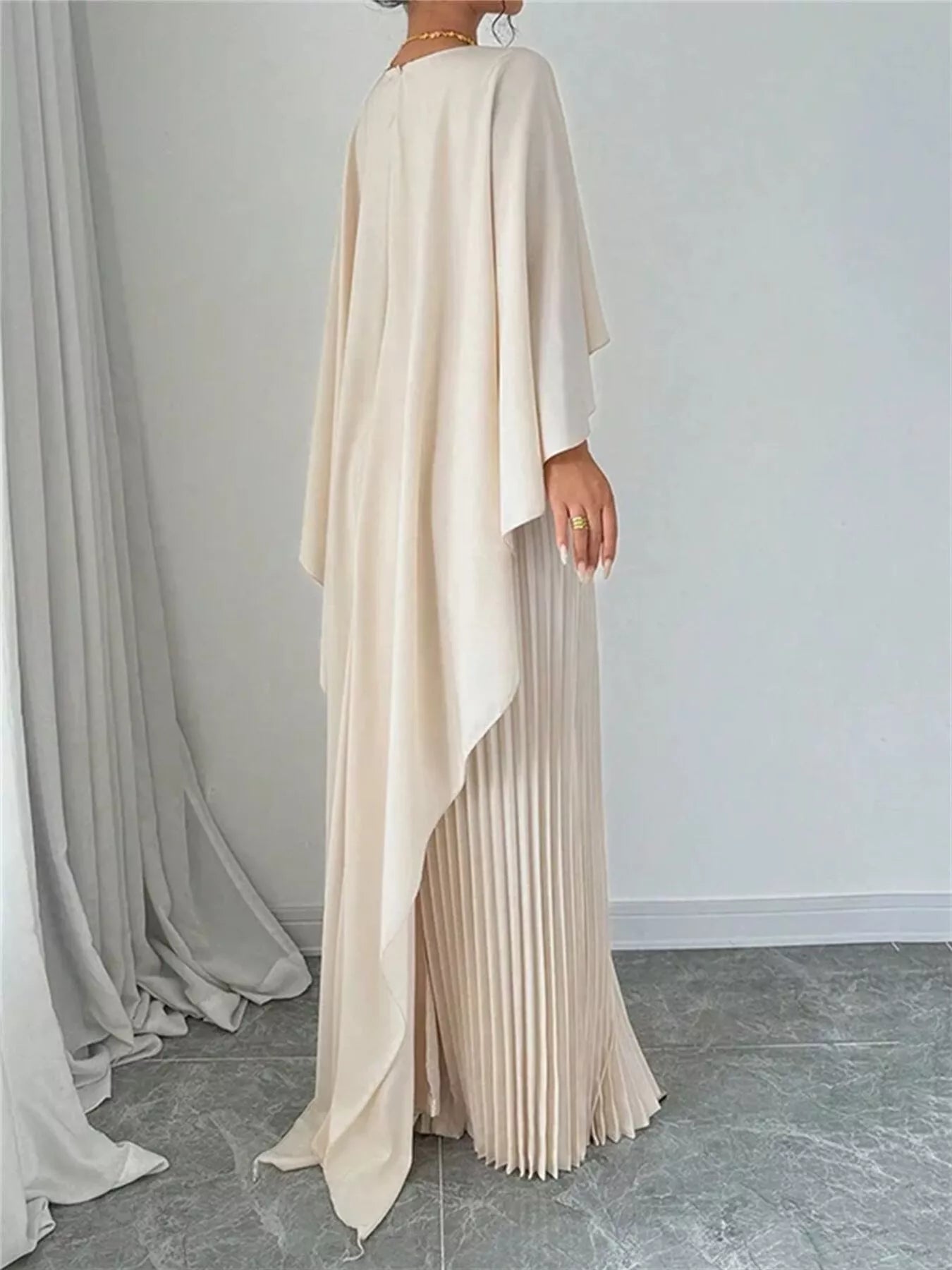 Cream cape pleated maxi dress shown from back, draped cape and pleated long skirt