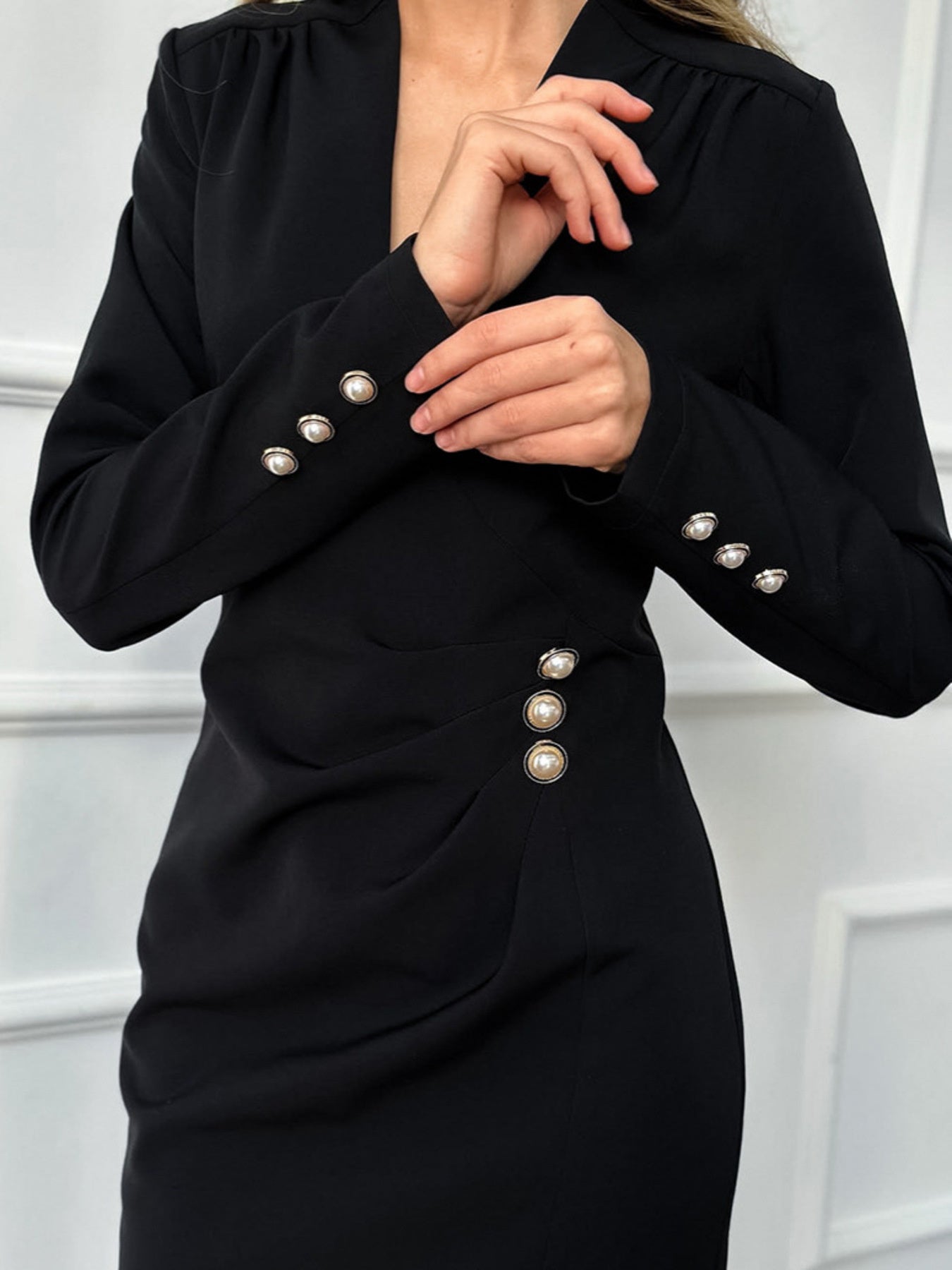 Black V-neck long-sleeve dress with ruched seams and pearl button details on sleeves.
