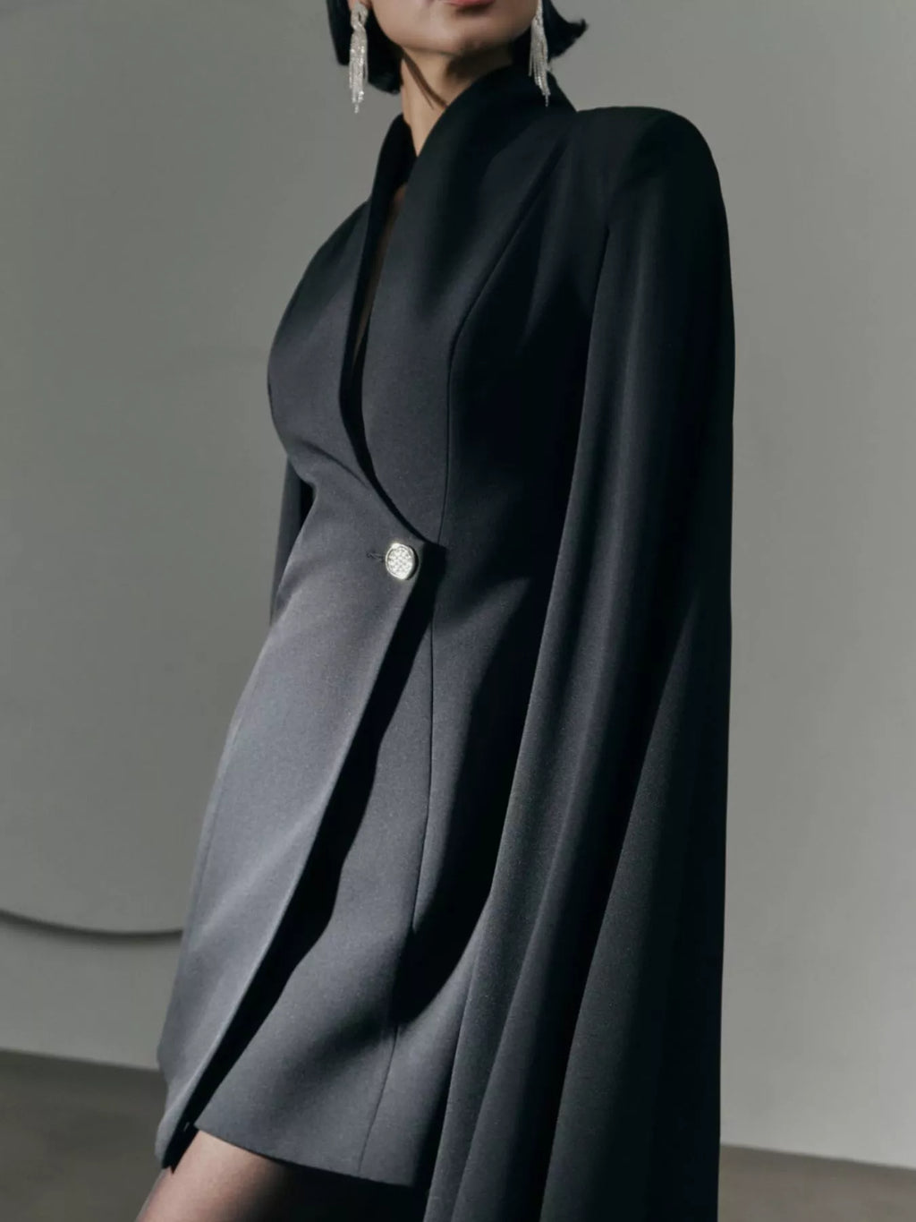 Black mini blazer dress with cape sleeves and one-button front; close side view