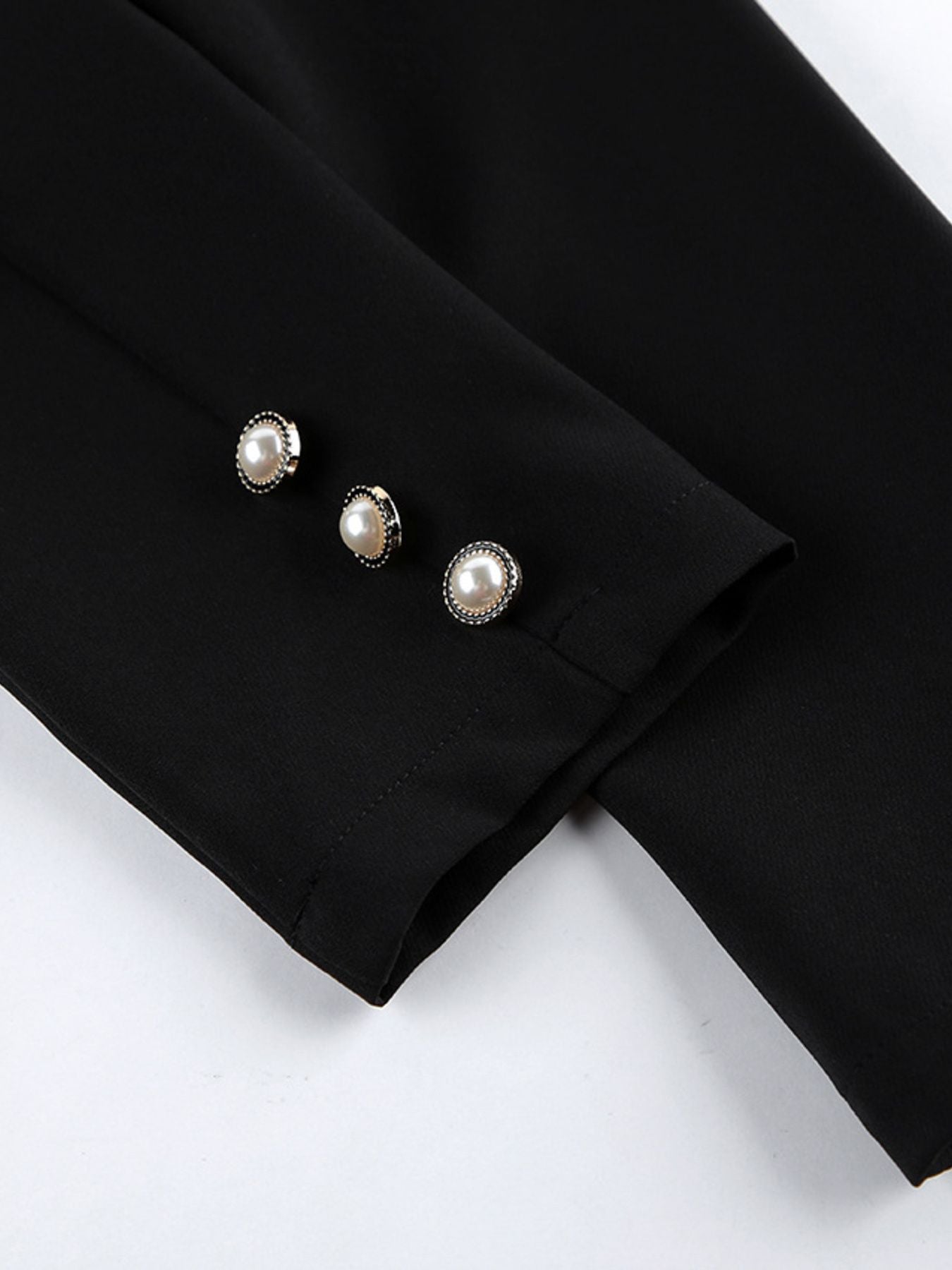 Black long-sleeve cuff with three pearl button accents and subtle seam stitching.