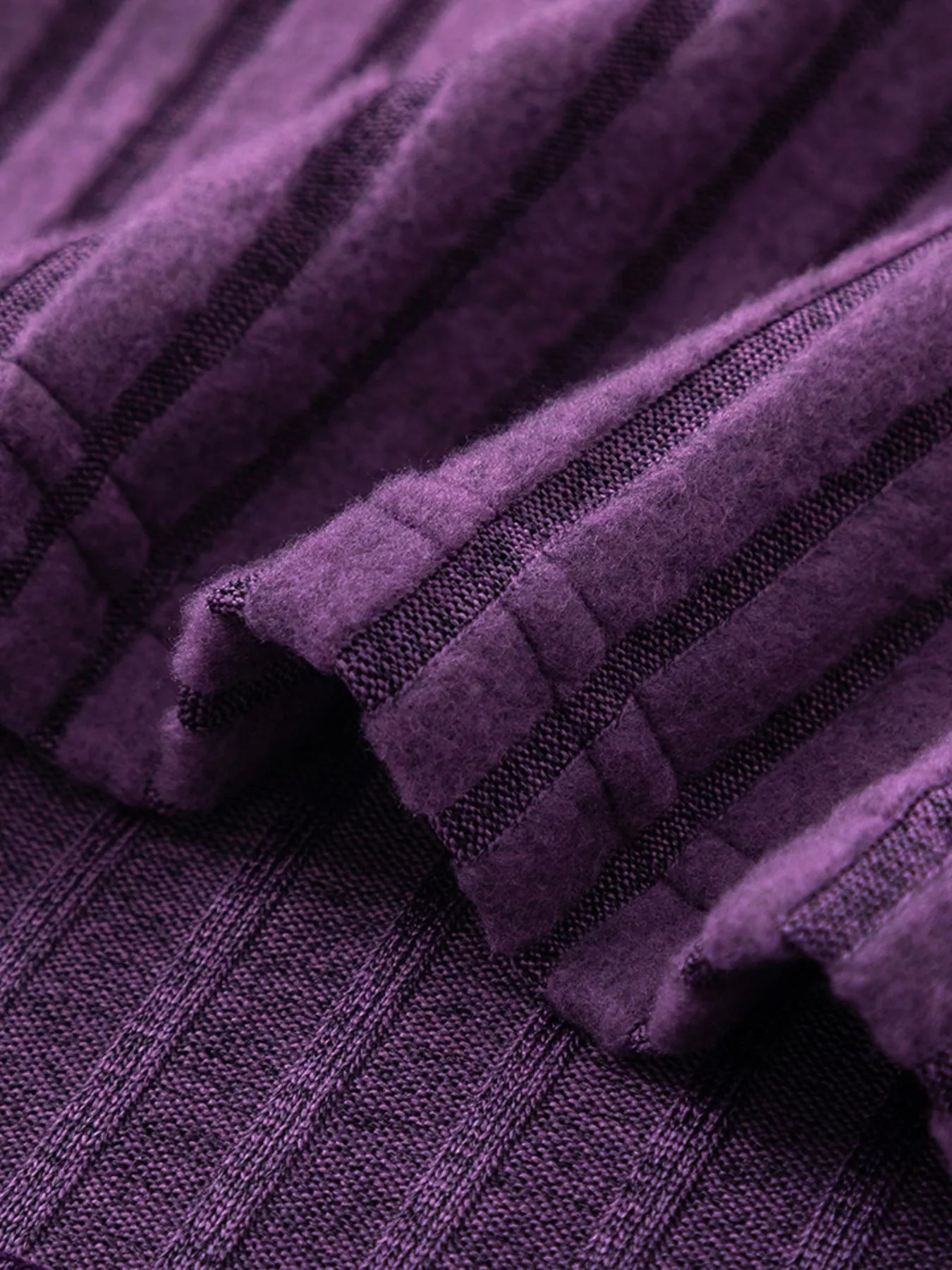 Purple ribbed knit fabric fold with seams, zipper pull partially visible