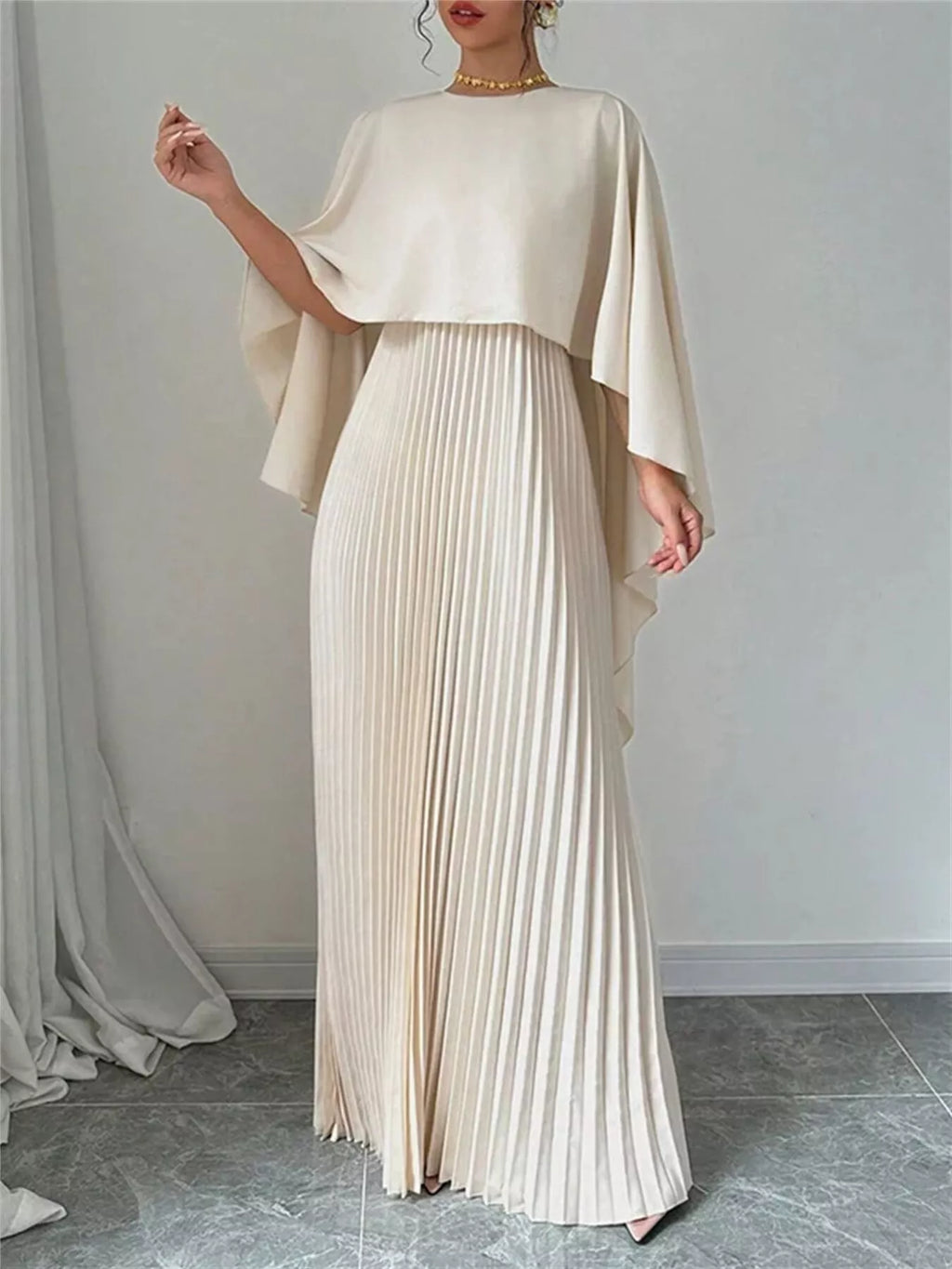 Cream cape pleated maxi dress with flowing cape sleeves and vertical pleated skirt