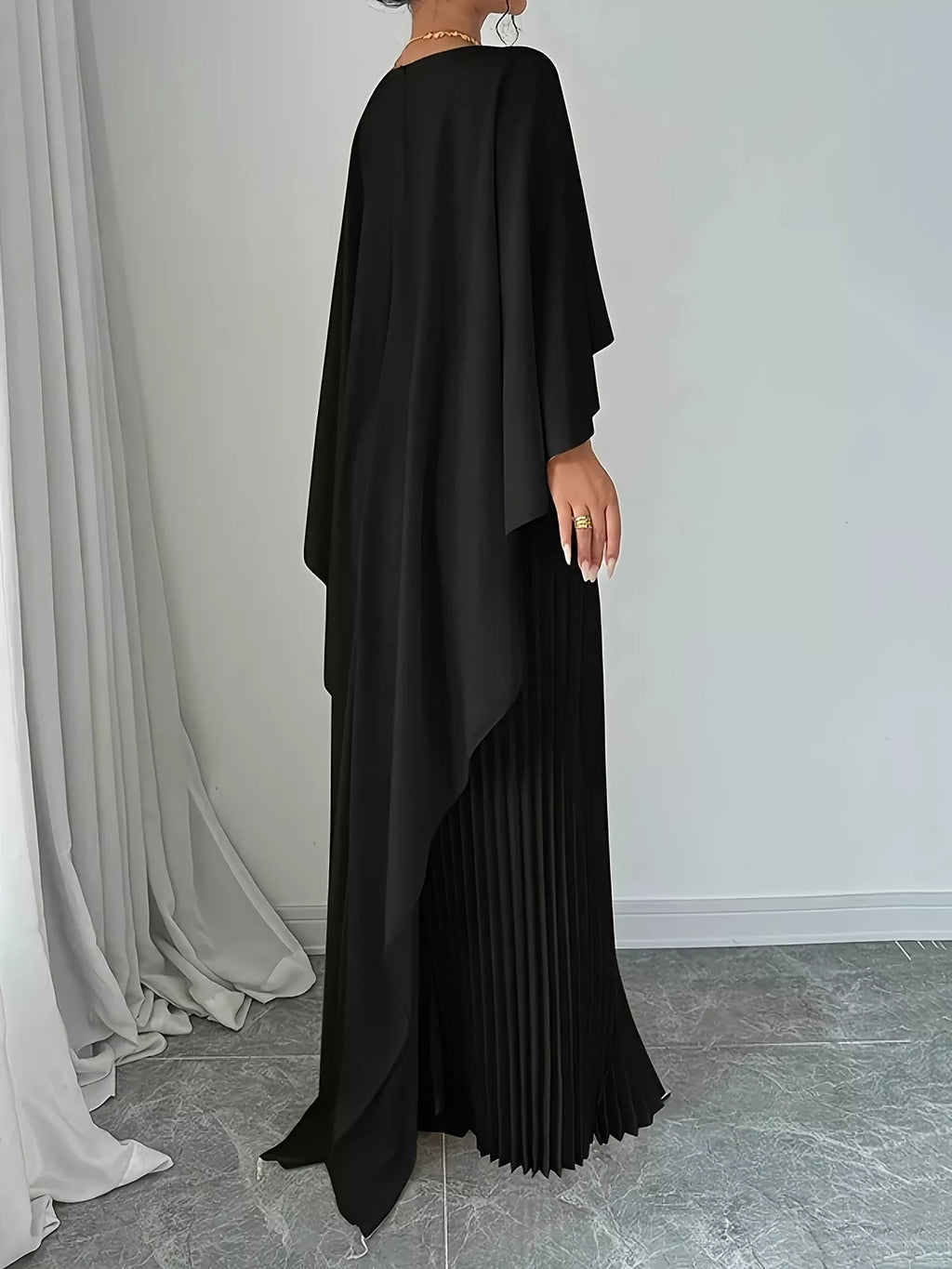 Black cape pleated maxi dress shown from back with draped cape and pleated long skirt