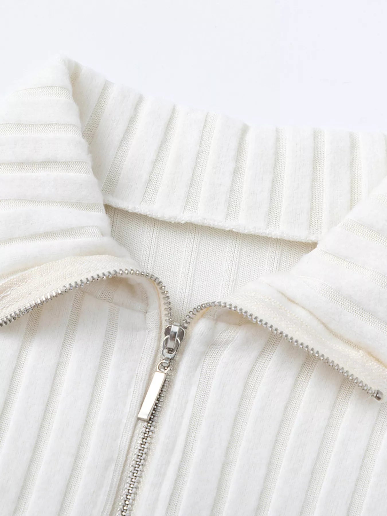 White ribbed knit half-zip area with metal zipper pull and stand collar