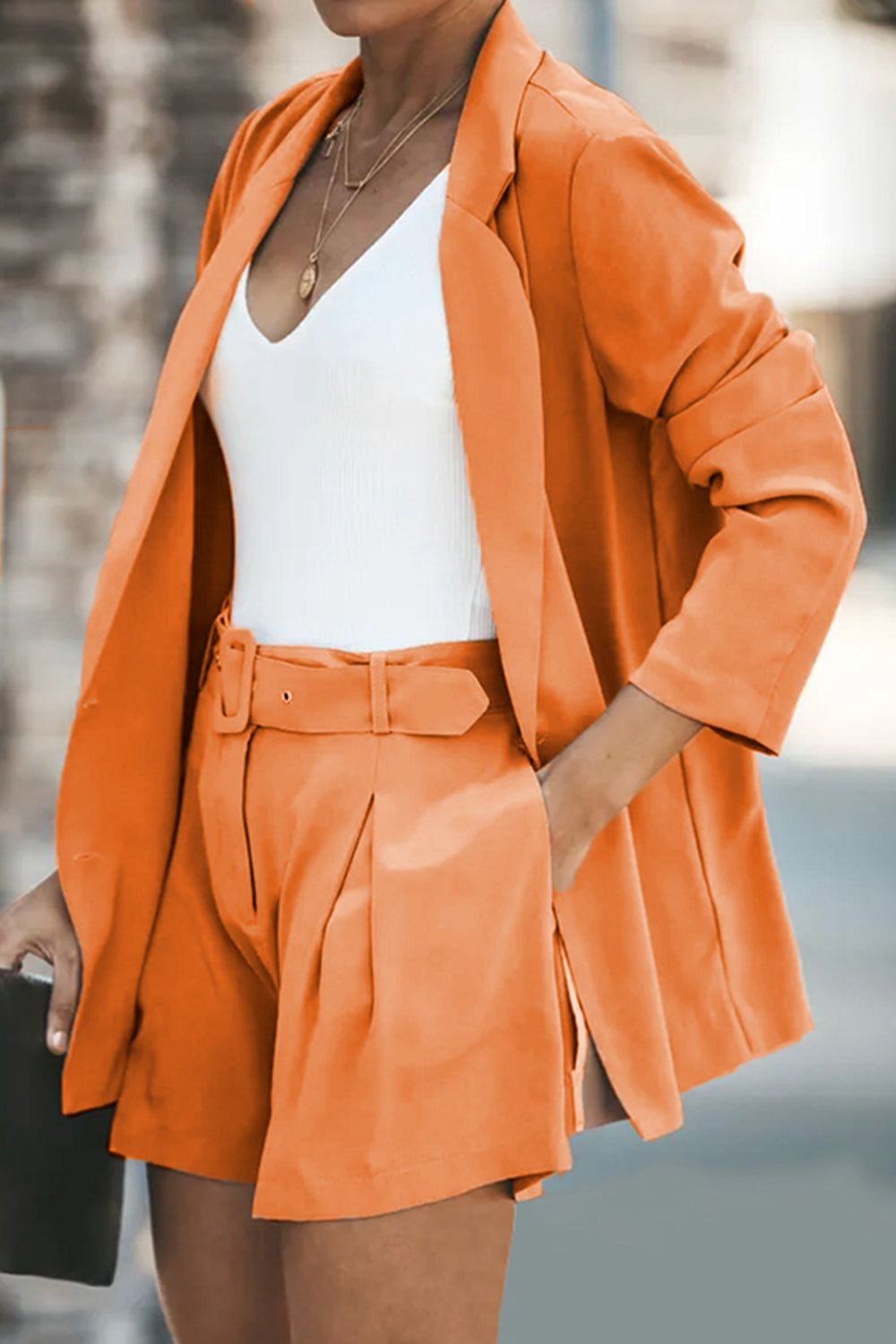 Two-piece blazer and shorts set in orange; long blazer with flap pockets, belted tailored shorts.