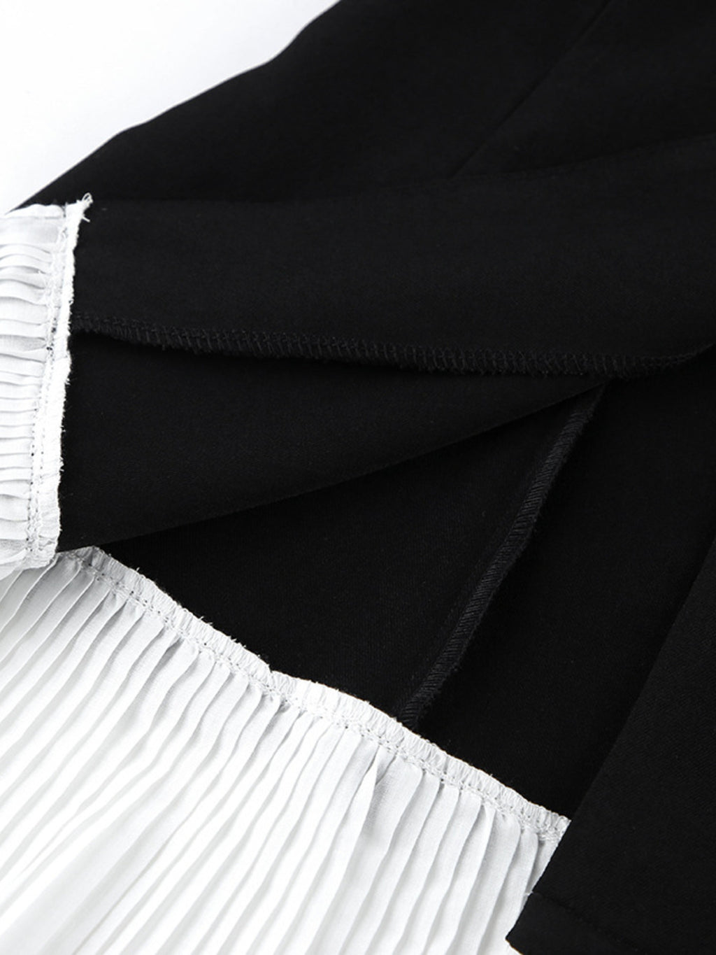 Black blazer dress with one-button bodice and pleated skirt, close-up of waistband