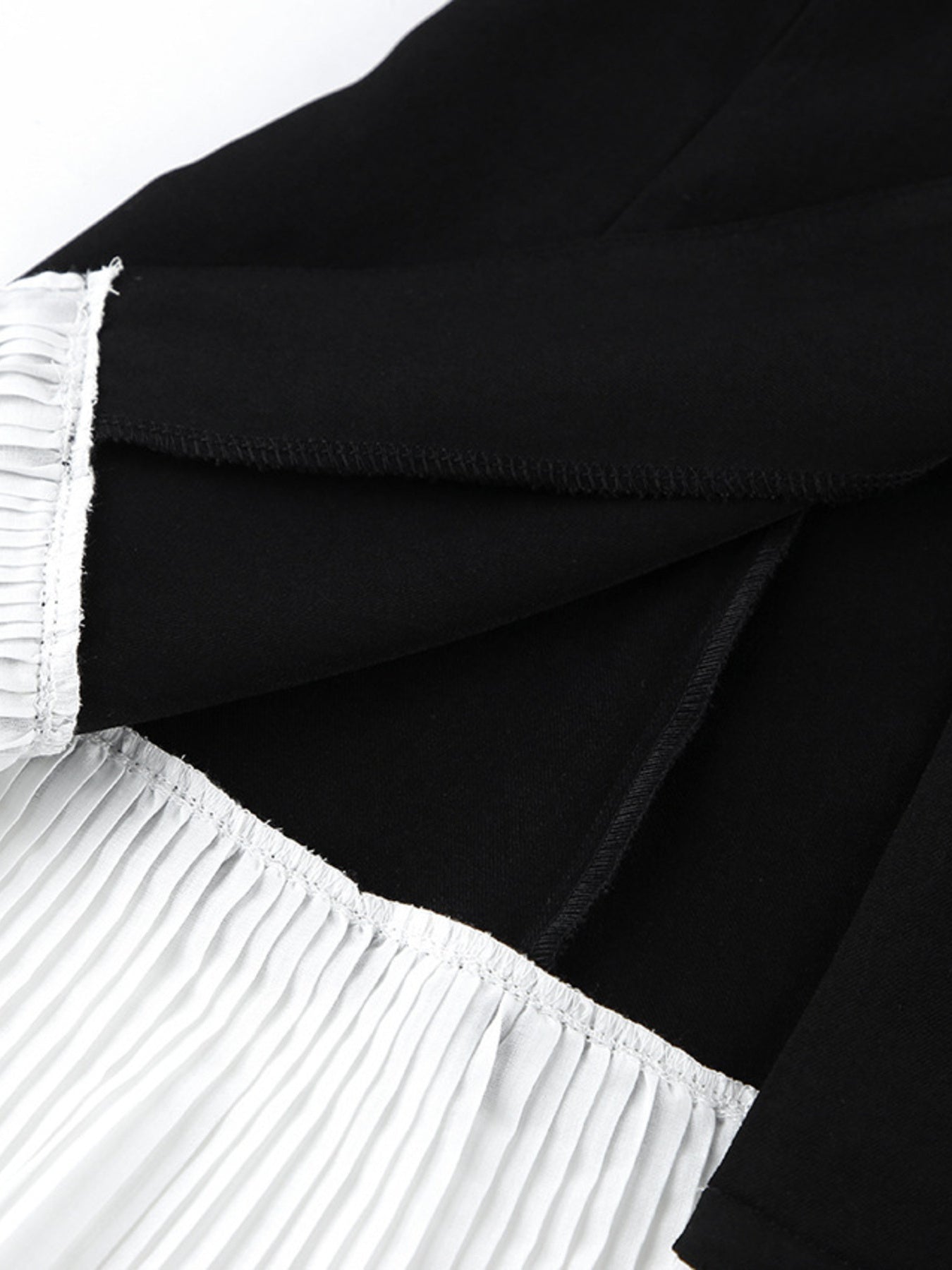 Black blazer dress with one-button bodice and pleated skirt, close-up of waistband