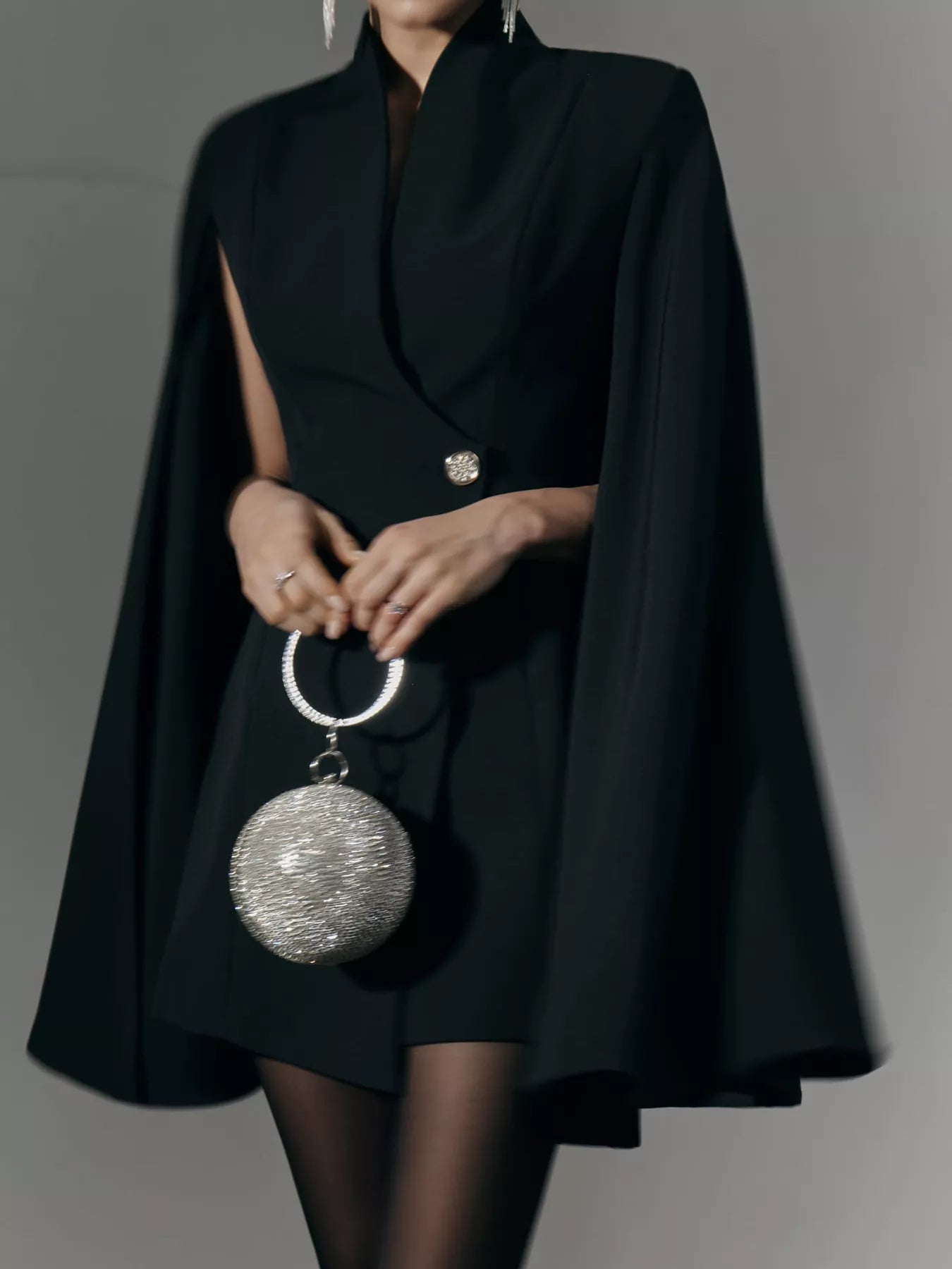 Black one-button fitted mini blazer dress with cape sleeves; hands holding small bag