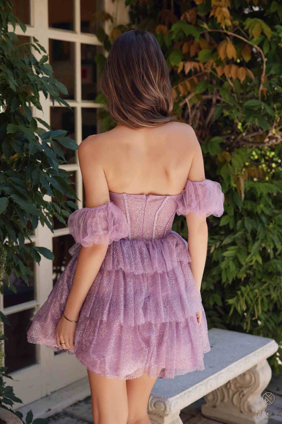 Back view of a woman in Nox Anabel Y860 strapless A-line dress with detachable cuffs, showcasing the glitter tiered design.